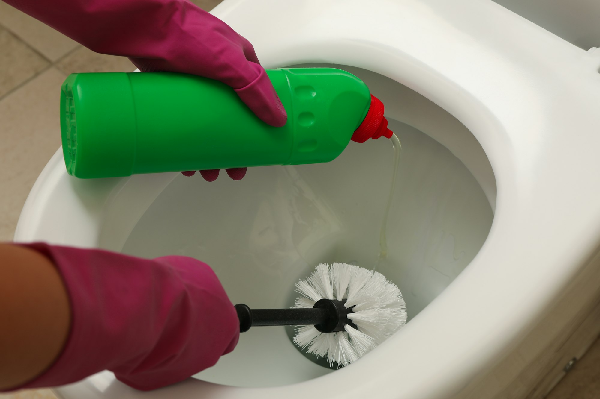 Woman in rubber pink gloves cleans toilet bowl with brush