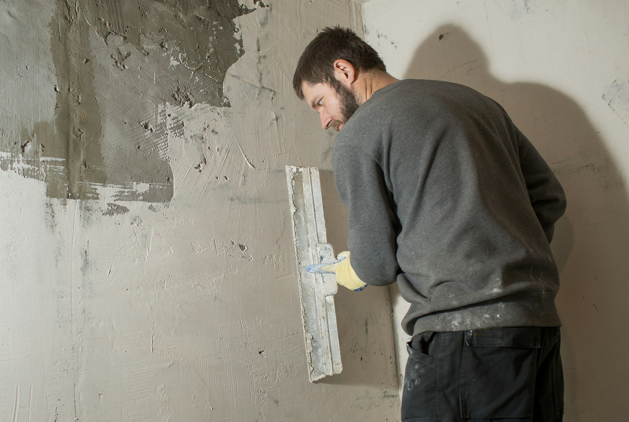 a male plasterer plasters a concrete wall with a spatula.