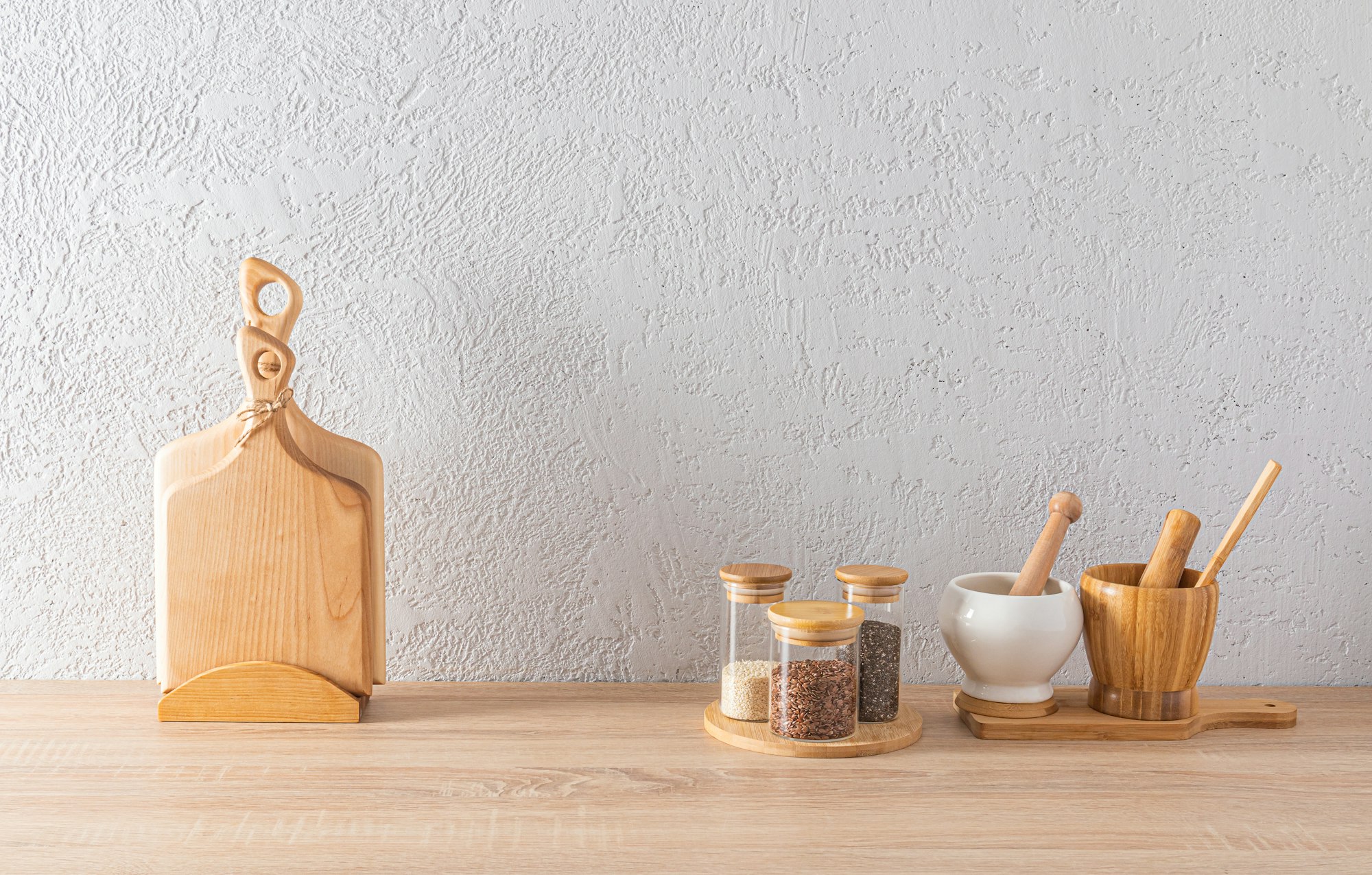 A set of glass spice jars, two mortars with a pestle,cutting wooden boards on the kitchen countertop