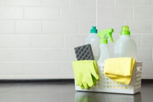 Mand met afwasmiddelen, handschoenen en sponzen op keukentafel. Onschadelijk afwasmiddel