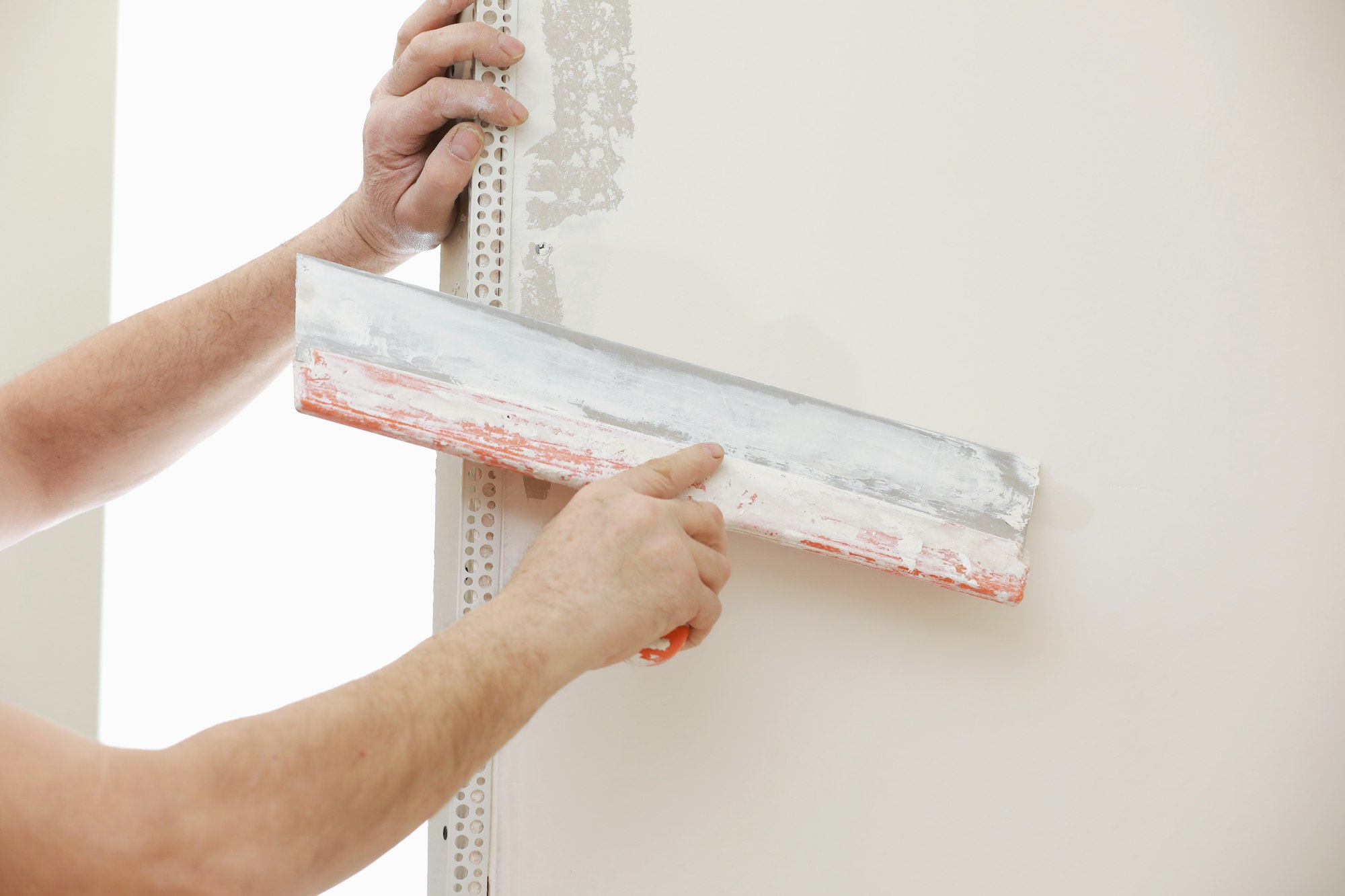 Builder in protective mask using a trowel to add plaster. Plastering wall with putty-knife, close up