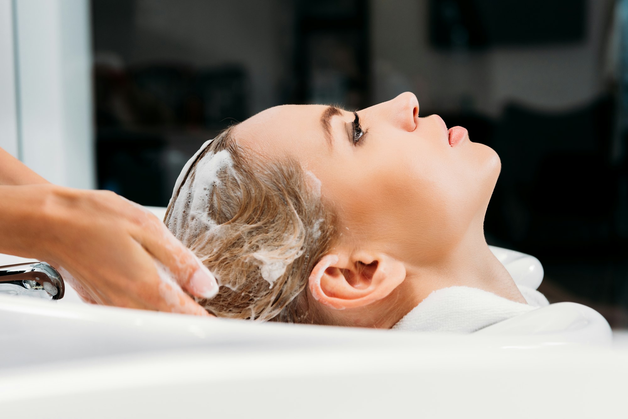 side view of hairdresser washing hair for customer with shampoo